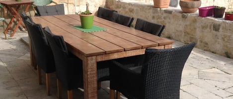 Ein Holztisch mit schwarzen Stühlen, umgeben von Blumentöpfen und Gartenmöbeln.