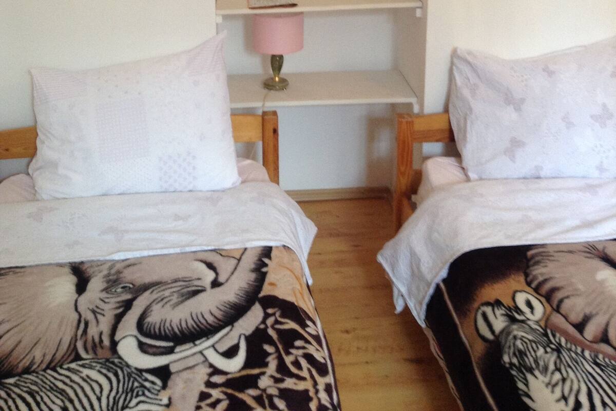 A bedroom with two beds, a bookshelf, and a lamp.