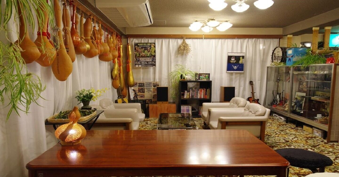 A living room with a wooden coffee table, two white sofas, a bookshelf, and a guitar.