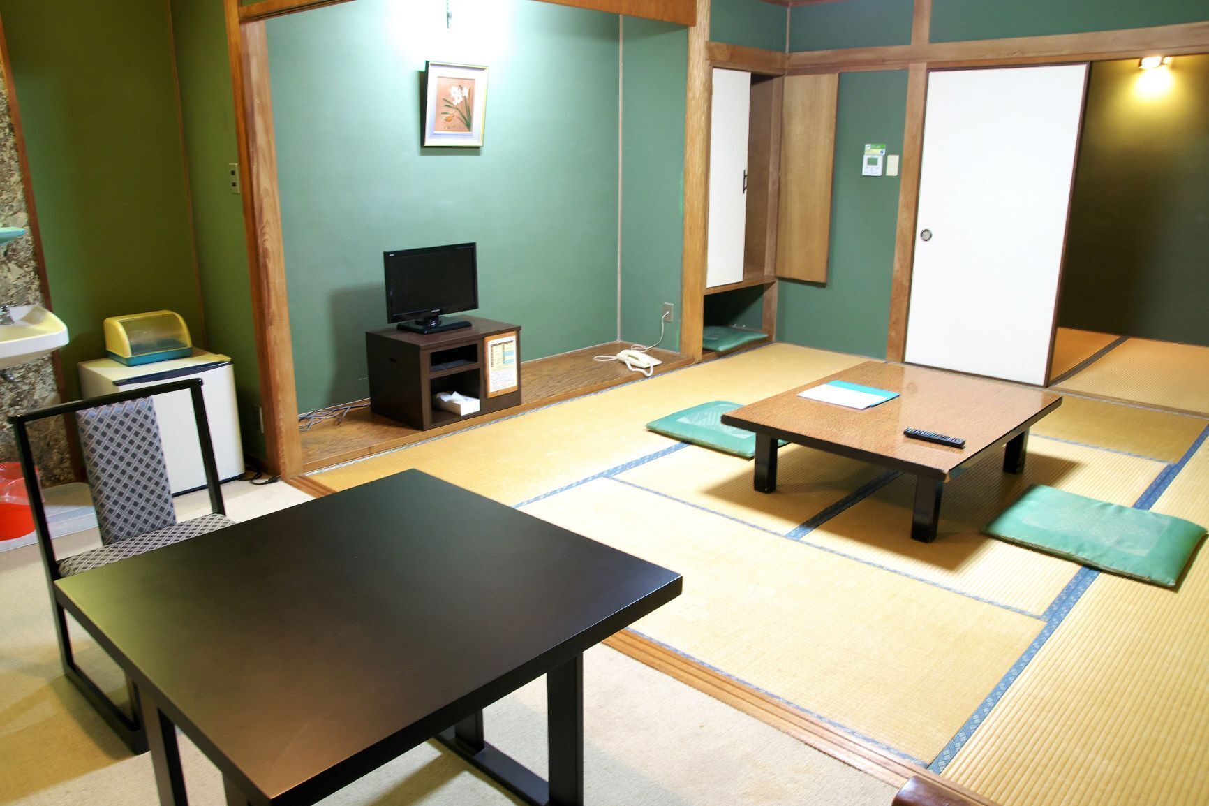 A tatami mat room with a low table, a television on a small stand, and a wooden wardrobe.