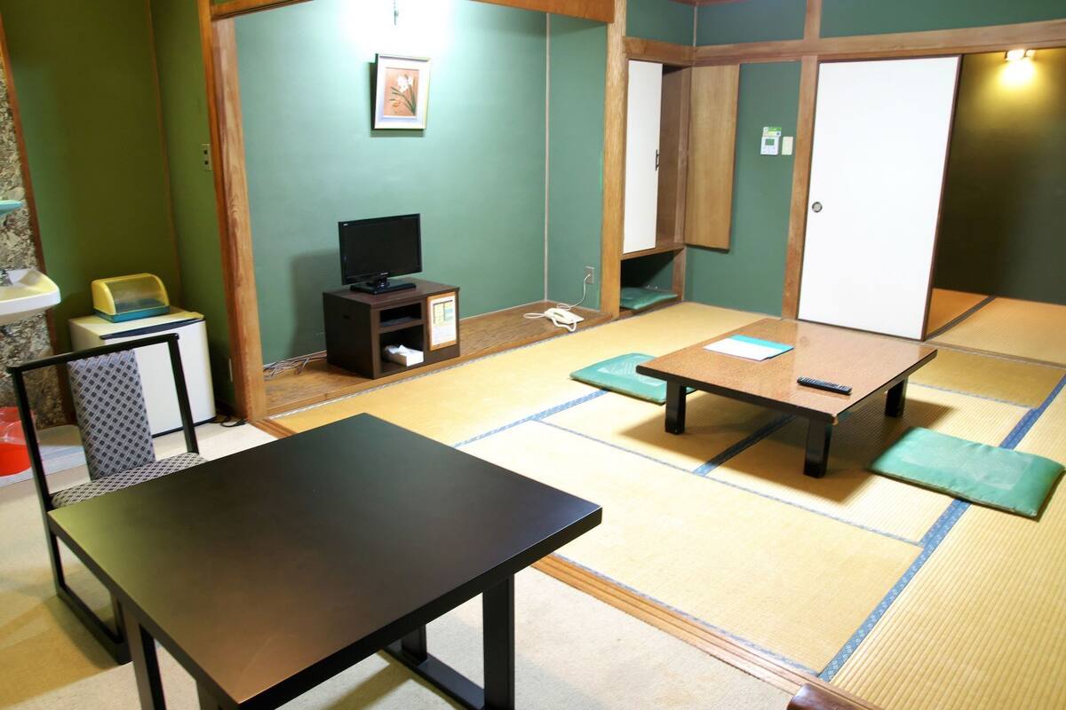 A tatami mat room with a low table, a television on a small stand, and a wooden wardrobe.