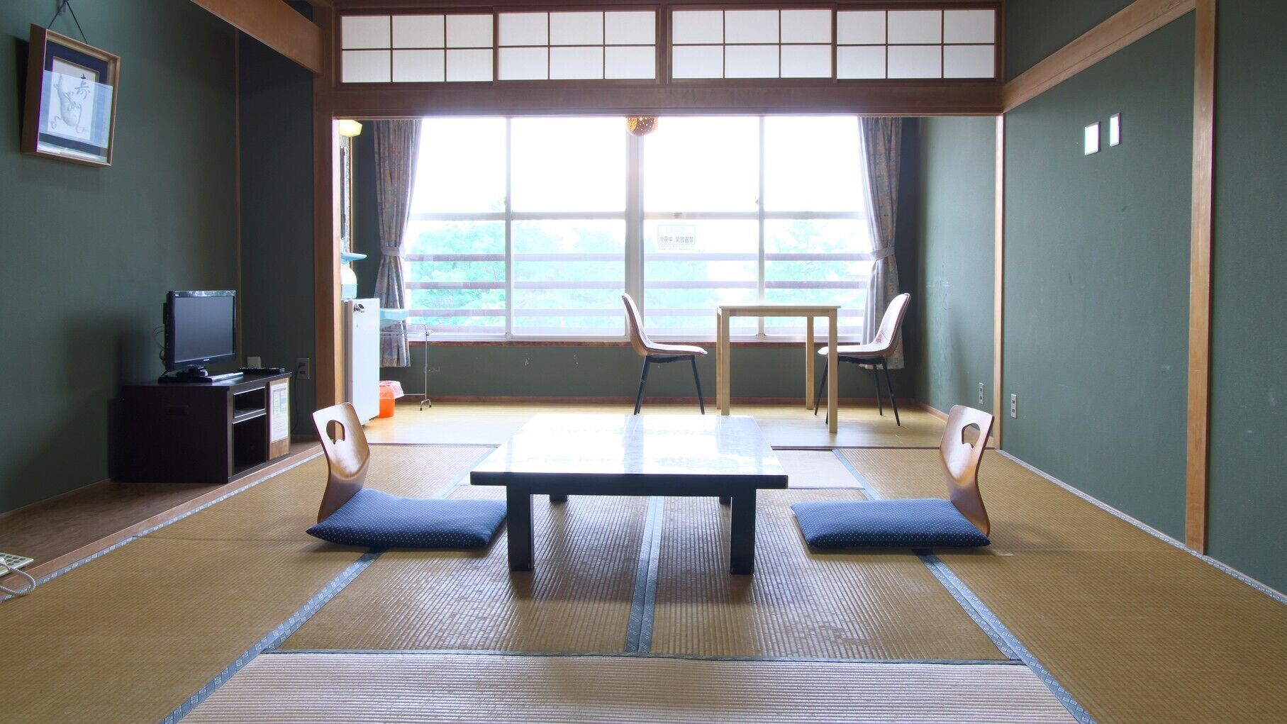 A tatami mat room with a television, a table, and chairs.