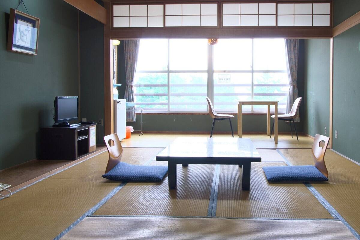 A tatami mat room with a television, a table, and chairs.