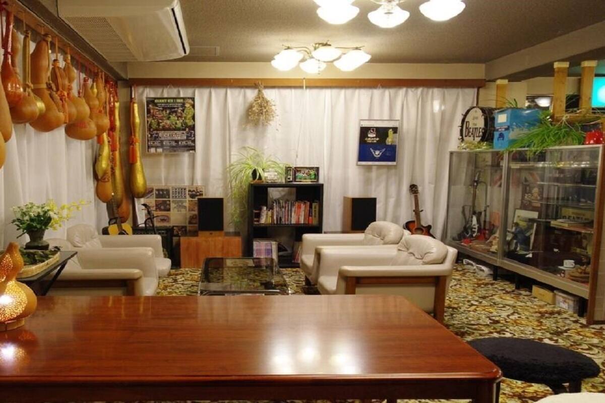 A living room with a wooden coffee table, two white sofas, a bookshelf, and a guitar.