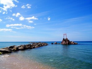 A rocky shoreline with clear water and a red structure on a rock. - Ryokan Suigou (Yurihama)