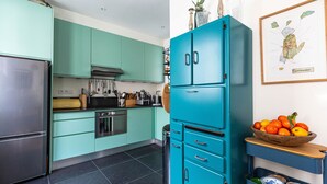 A kitchen with teal cabinets, a stainless steel refrigerator, and a wooden bowl of fruit on a wooden shelf. - Colour in Ternes, by Veeve (Paris)
