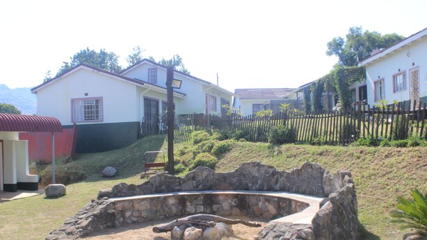 A stone structure in a garden with houses in the background. - African Violet (Mbabane)