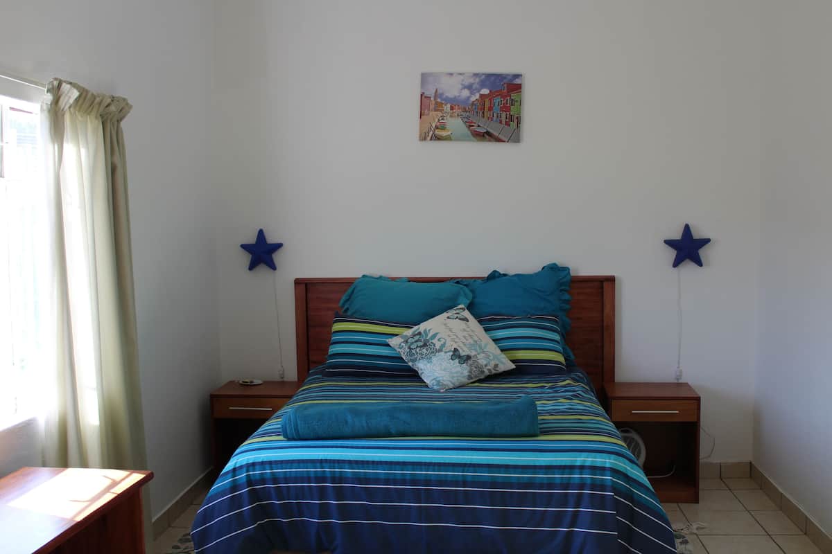 A bedroom with a bed, two bedside tables, a nightstand, a window with curtains, and a wall-mounted star decoration.