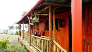 A wooden cabin with a porch, a hanging plant, and a view of the landscape.