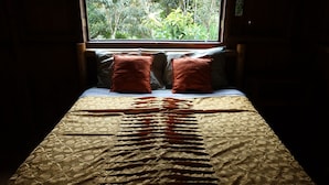 A bed with a patterned bedspread and two pillows, positioned in front of a window with a view of greenery.