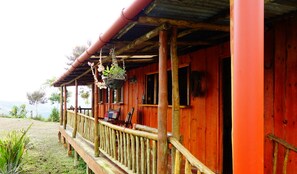 Eine Holz-Blockhütte mit Veranda, einer hängenden Pflanze und Blick auf die Landschaft.