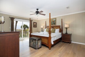 Una cama con dosel y tablero de madera, una mesita de noche con lámpara, otra mesilla y vistas al exterior a través de una puerta corredera.