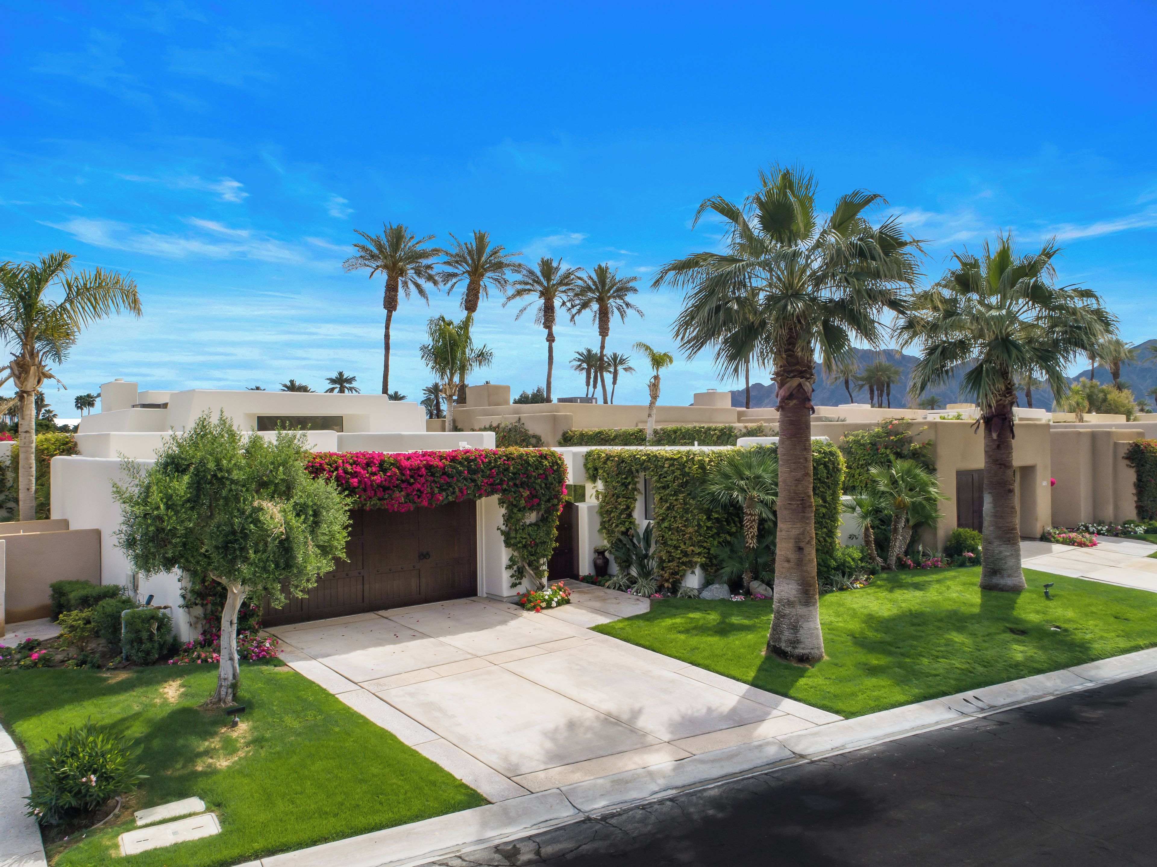 A residential area with modern architecture, palm trees, and a well-maintained lawn.