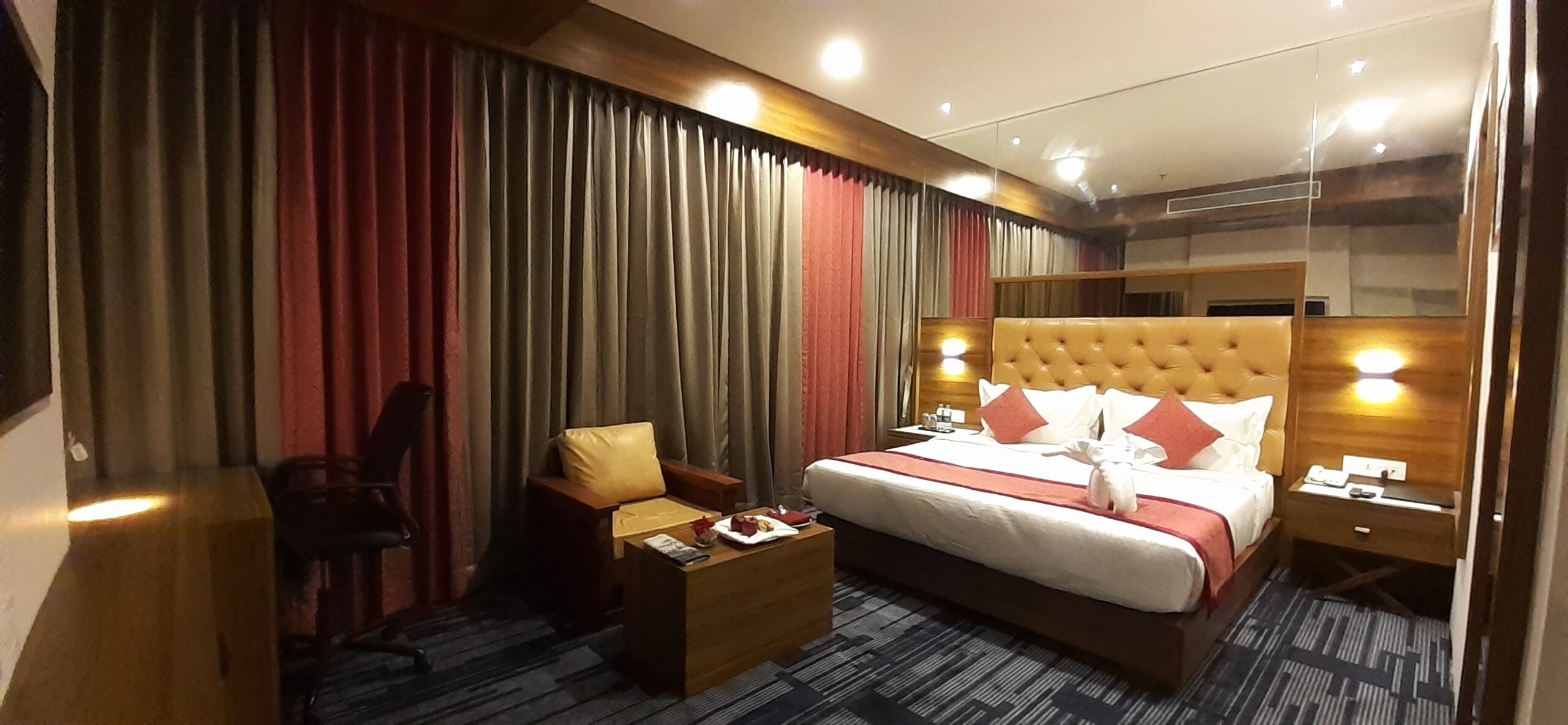 A hotel room with a large bed, a desk, a chair, and a mirror.