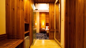 A wooden hallway leading to a room with a bed, a desk, and a lamp.