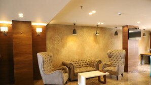 A lobby with two tufted armchairs, a white coffee table, and wall-mounted lamps.