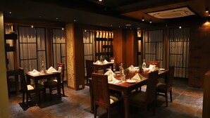 A dining area with wooden tables and chairs, curtains, and a brick wall.
