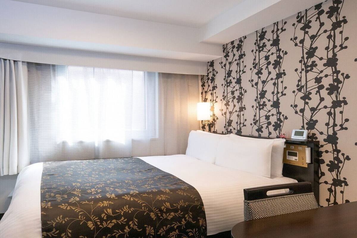 Ein Hotelzimmer mit einem Bett, einem Nachttisch mit Lampe, einem Fernseher und einer Wand mit Blumenmuster.