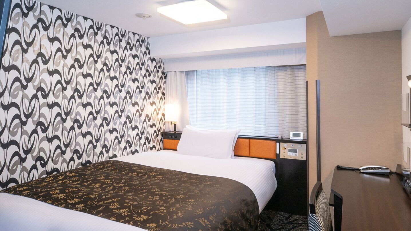 Una habitación de hotel con cama, escritorio, teléfono y ventana con persianas.