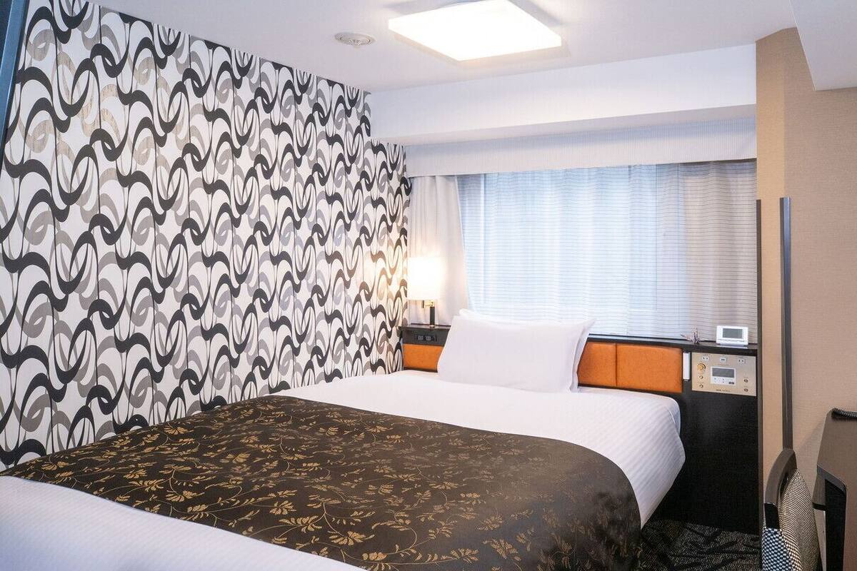 Una habitació d'hotel amb un llit, una taula de treball, un telèfon i una finestra amb persianes.
