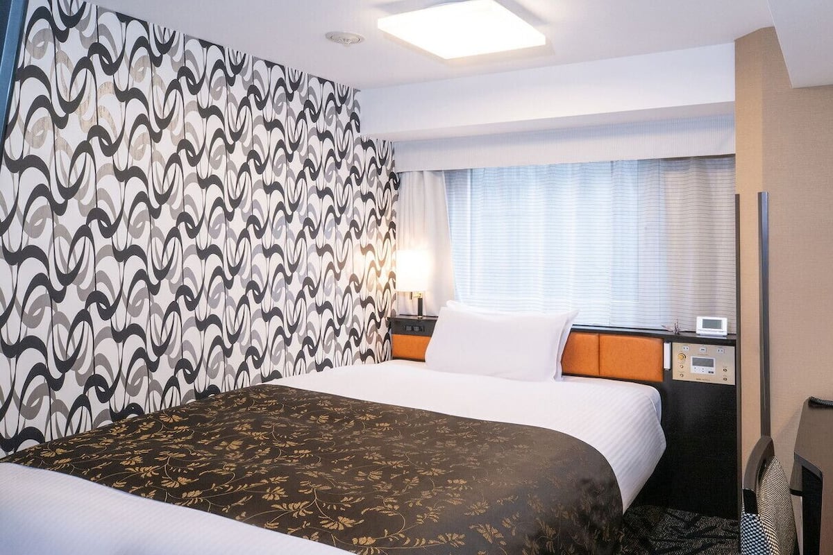 Ein Hotelzimmer mit Bett, Schreibtisch, Telefon und einem Fenster mit Jalousien.