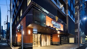 A modern building with 'APA HOTEL' signage, featuring a prominent entrance and a well-lit facade.