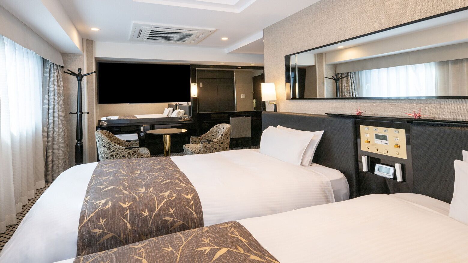 Una habitación de hotel con dos camas, un escritorio, una silla, un espejo y un panel de control.