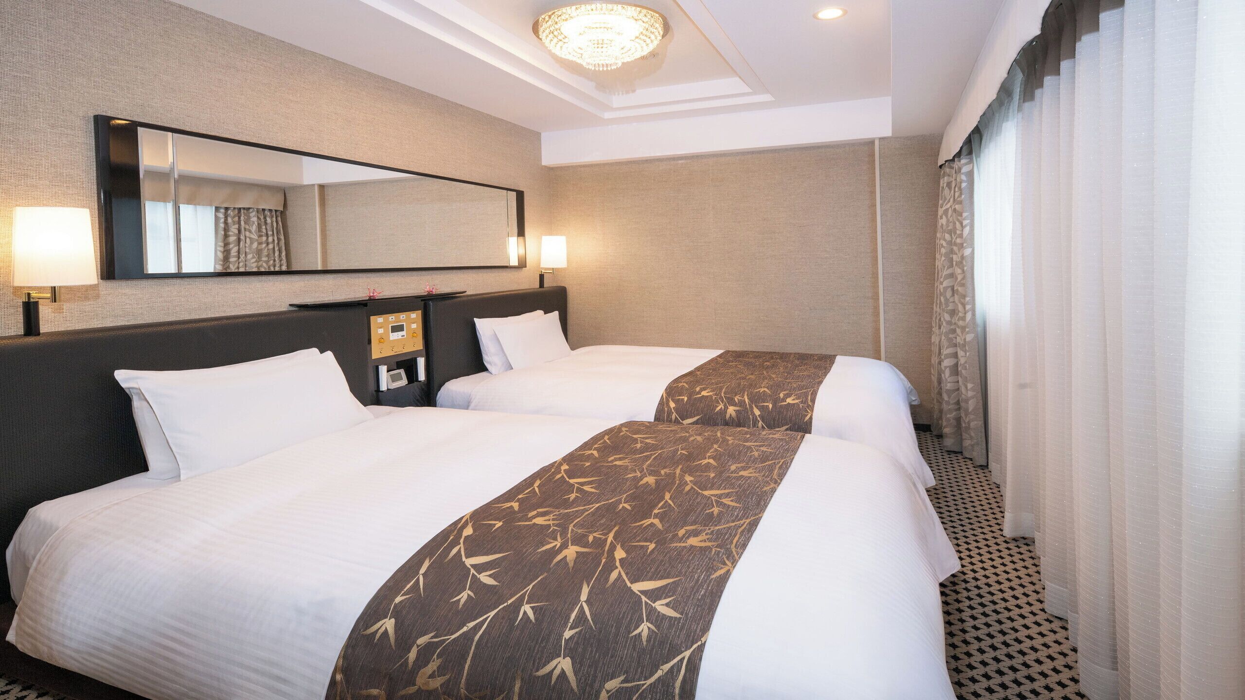Ein Hotelzimmer mit zwei Betten, einer Bedienkonsole, einem Spiegel und einem Fenster mit Vorhängen.