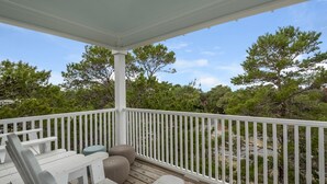 Eine überdachte Terrasse mit weißen Geländern, einem Holztisch und zwei runden Hocker.
