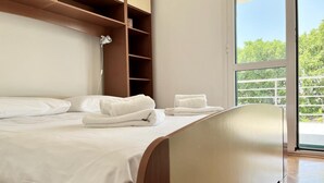A modern hotel room with a large bed, wooden headboard, and a view of greenery through a large window. - Lemon Tree Apartments (Zadar)