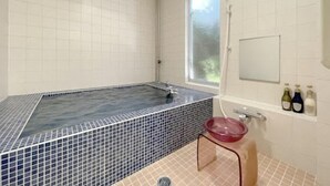 Een badkamer met een groot bad, een raam en een wastafel met flessen.