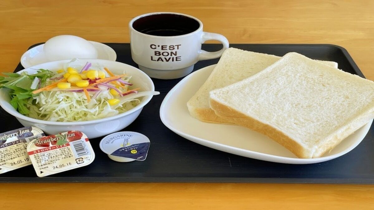 Ein Tablett mit einem Sandwich, einer Tasse, einem Salat und zwei Marmelapäckchen.