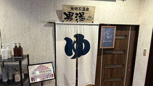 Een kamer met een houten deur, een wit gordijn met een groot blauw symbool, een bordje voor een Shampo Bar, en een plank met toiletartikelen.