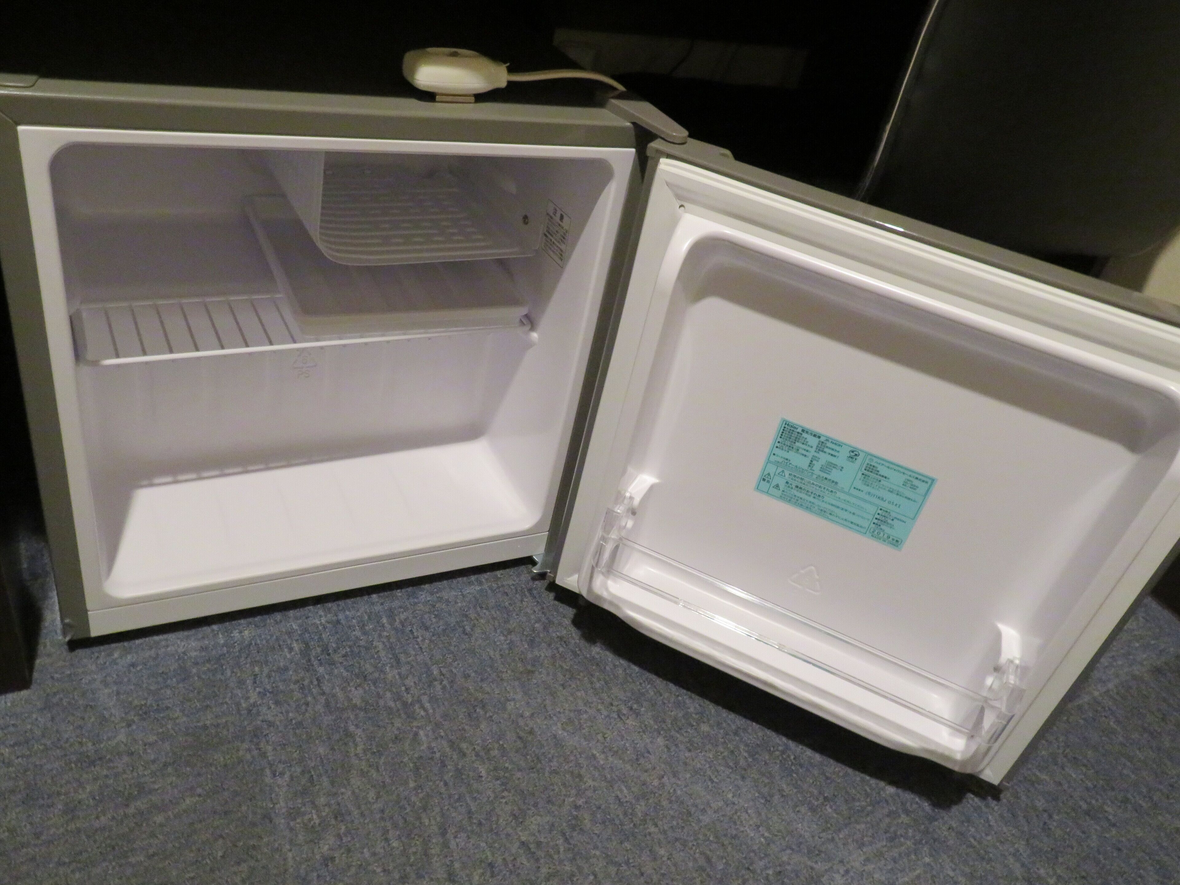 An open refrigerator with a label on the door, a power cord, and a tray inside.