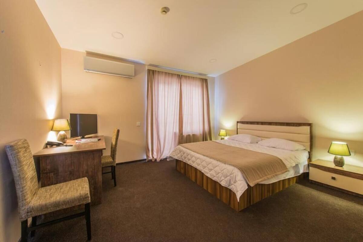 A hotel room with a bed, a desk, a chair, a TV, and a window with curtains.