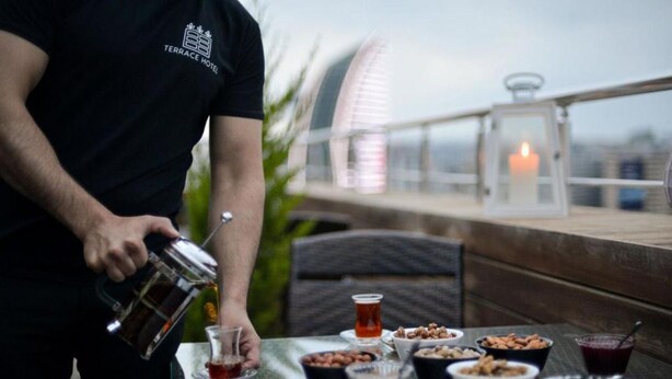 A person pouring a drink into a glass on a terrace with a table set with various food items and a candle. - Check-in TERRACE Hotel (Baku)