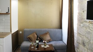 A living room with a grey sofa, two brown cushions, a small wooden table with a bottle of wine and two glasses, and a vase with flowers.