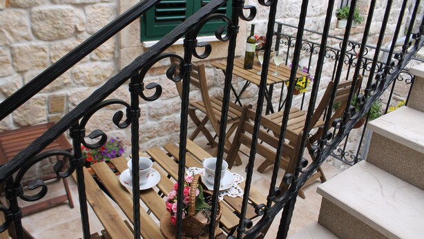 A stone building with a wooden table set for two, a wicker basket with flowers, and a bottle of wine.