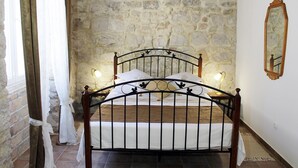 A bed with a metal frame, white bedding, and two bedside lamps. The room has a stone wall and a wooden ceiling.