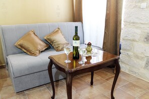 Une pièce avec un canapé gris, une table basse en bois, une bouteille de vin, deux verres à vin et un vase rempli de fleurs.