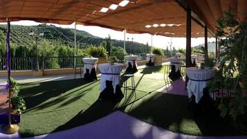 Terraza al aire libre con mesas y sillas, rodeada de vegetación y colinas.