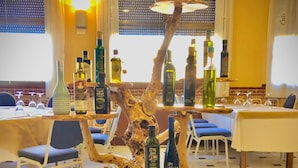 A restaurant interior with a central wooden sculpture holding bottles, tables with chairs, and a tiled floor. - Hotel Avenida (Beas de Segura)