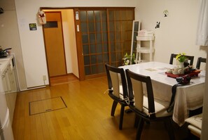 A dining area with a wooden floor, a table with chairs, a white cabinet, and a sliding door with a frosted glass panel.