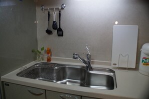 A kitchen with a double stainless steel sink, a hanging utensil rack, a small potted plant, and a white appliance on the counter.