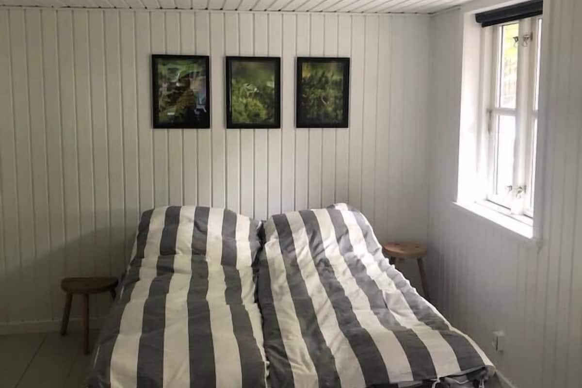 A bedroom with a bed, a ceiling fan, a window, and three framed pictures on the wall.
