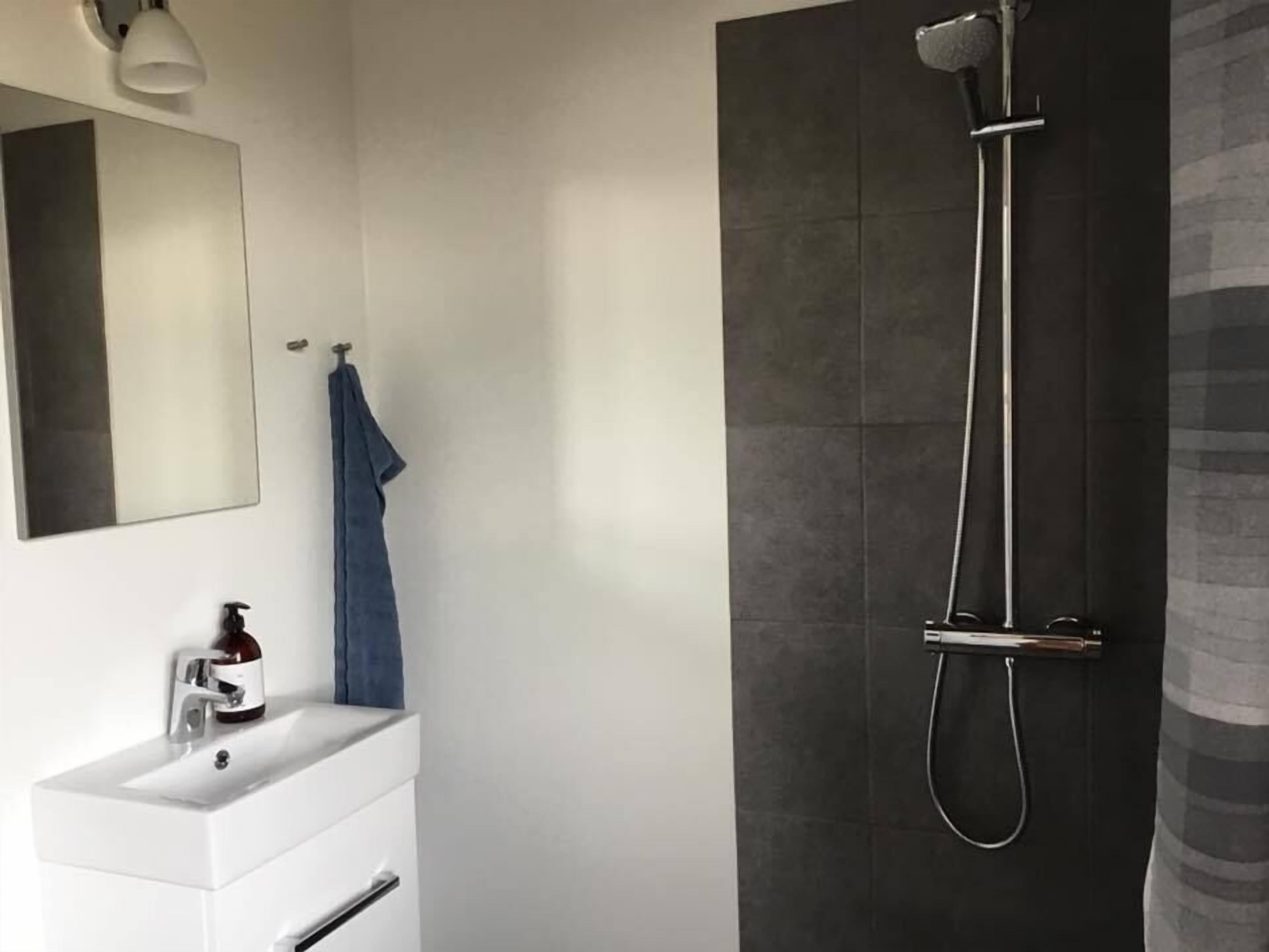 A modern bathroom with a white vanity, a large mirror, a towel hanging on the wall, and a shower with a handheld showerhead.