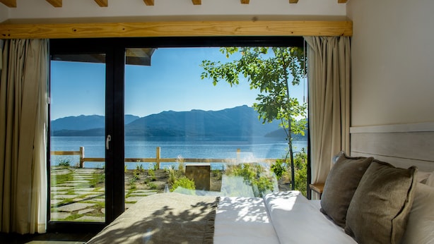 A bedroom with a large sliding glass door leading to a balcony overlooking a lake and mountains. - Correntoso TownHouses (Villa La Angostura)
