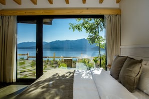 Quarto com uma grande porta de correr de vidro que dá para uma varanda com vista para um lago e montanhas.
