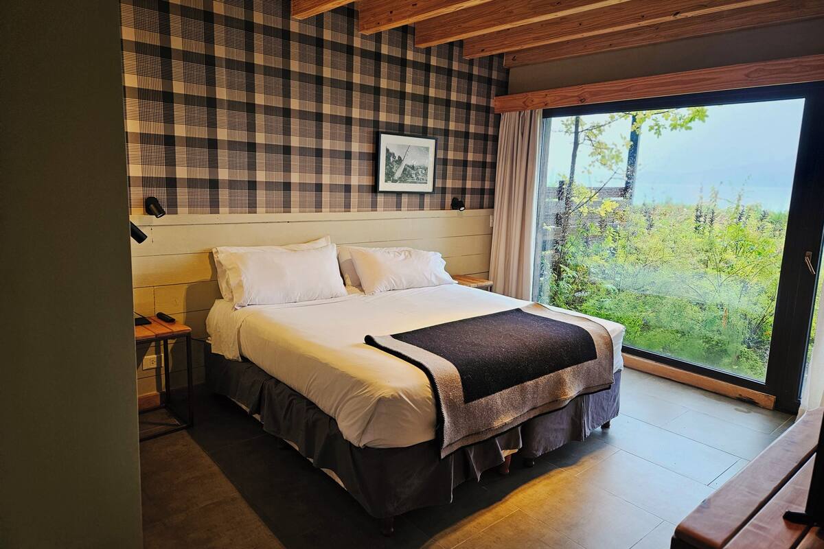 A bedroom with a bed, bedside tables, a window with a view, and a checkered wall pattern.