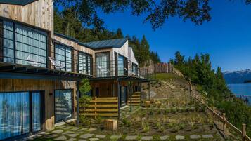 A modern wooden building with large windows and a stone pathway leading to a lake.